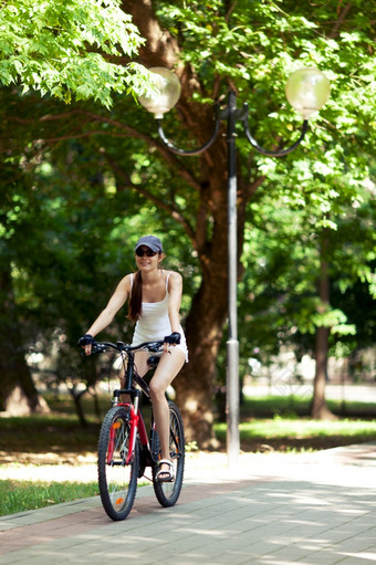 女孩骑自行车的公园她rsquo穿白色体育运动衣服帽她的自行车红色的rsquo阳光明媚的夏天一天