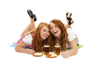 两个笑巴伐利亚女孩与啤酒而且椒盐卷饼的地板上两个笑巴伐利亚女孩与啤酒而且椒盐卷饼的地板上白色背景