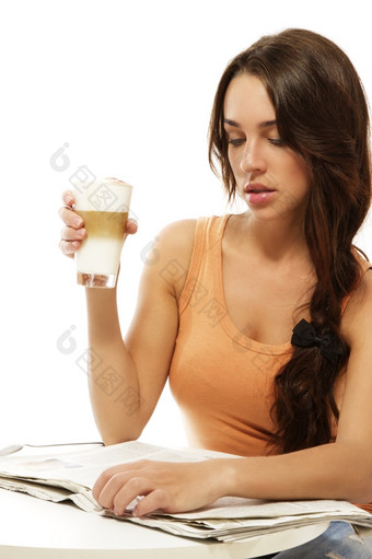 年轻的女人坐着表格阅读报纸持有拿铁<strong>玷污</strong>咖啡年轻的女人坐着表格阅读报纸持有拿铁<strong>玷污</strong>咖啡白色背景