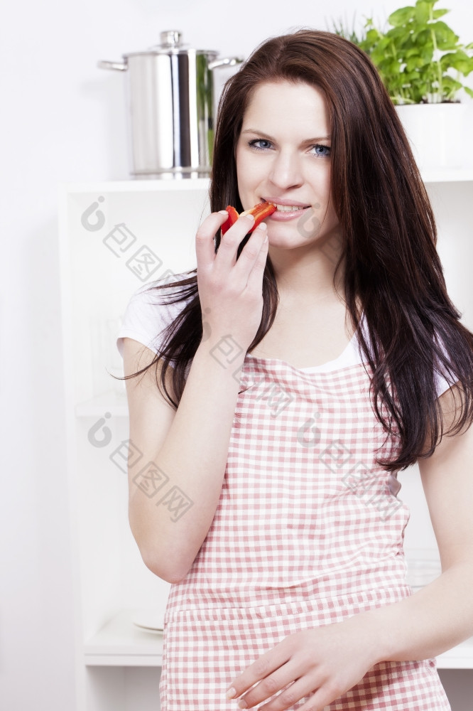年轻的女人吃红辣椒年轻的微笑女人吃红色的红辣椒她的厨房
