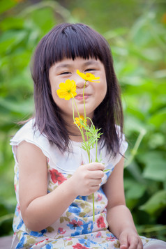 亚洲孩子们坐着花园与黄色的宇宙花手
