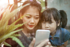 亚洲年轻的女人和孩子们看聪明的电话屏幕首页生活房间