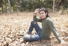 亚洲年轻的男人。坐着干叶子场与微笑脸
