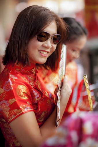 亚洲女人穿中国人传统西装和持有竹子风扇与露出牙齿的微笑脸曼谷中国小镇