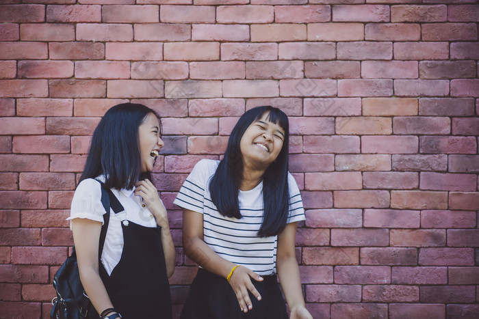 两个亚洲少年笑与幸福情感站对红色的砖墙