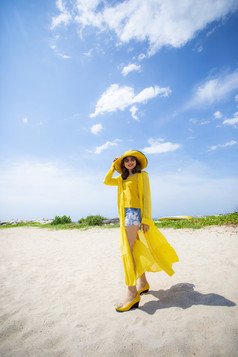 美丽的亚洲女人穿黄色的衣服站海海滩对中午太阳光