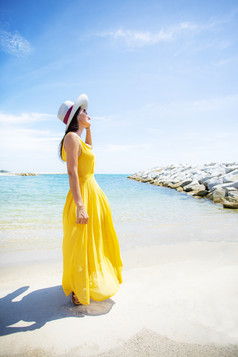 美丽的亚洲年轻的女人穿黄色的衣服放松夏天vacaiton海滩