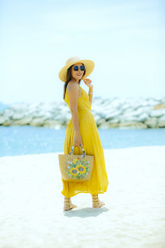 美丽的亚洲女人穿黄色的衣服站海海滩对中午太阳光