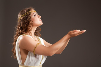 的美丽的年轻的女人穿白色而且黄金希腊服装持有某物她的手的黑暗背景