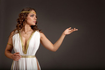 的美丽的年轻的女人穿白色而且黄金希腊服装看某物她的左的黑暗背景