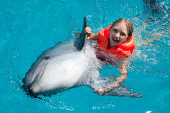 小微笑女孩游泳与的海豚的游泳池的明亮的阳光明媚的一天