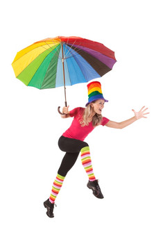 笑快乐年轻的女人跳与彩虹伞穿色彩斑斓的体育运动衣服而且色彩斑斓的帽子
