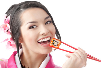 肖像的快乐年轻的日本女人吃寿司穿传统的和服衣服的白色背景