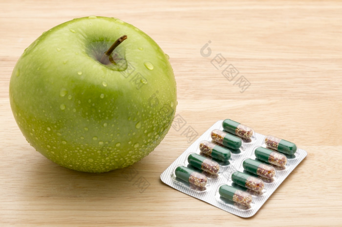绿色透明的药片胶囊和新鲜的绿色苹果绿色透明的药片胶囊和新鲜的绿色苹果木背景