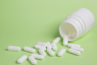 塑料白色瓶药片绿色背景分散白色药物塑料白色瓶药片绿色背景分散白色药片