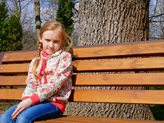 小美丽的高加索人女孩坐在的木板凳上的公园春天
