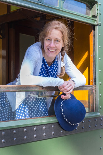 高加索人中间岁的女人穿着蓝色的<strong>老式</strong>的衣服持有帽子<strong>火车</strong>窗口
