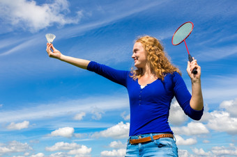 年轻的高加索人女人持有航天飞机和羽毛球球拍对蓝色的天空与白色云