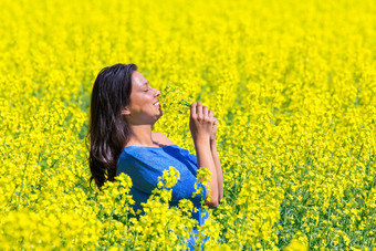 年轻的哥伦比亚女人闻黄色的花农业油菜籽场