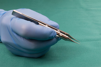 外科医生持有微外科手术toolSurgeon手蓝色的gloveSurgeon持有forcaps直与platformThe背景蓝色的桌布操作