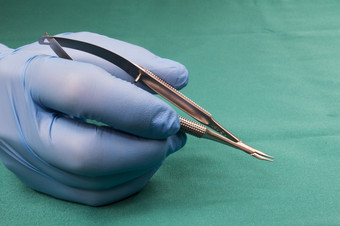 外科医生持有微外科手术toolSurgeon手蓝色的gloveSurgeon持有显微针持有人弯曲的短模型背景蓝色的桌布操作