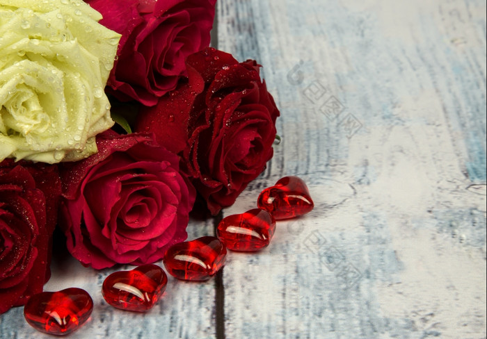 两个红色的两个栗色和一个白色玫瑰五个小红色的情人节心与露水滴蓝色的背景木板材与古董效果和空间为额外的文本水平viewon的正确的一边水平视图