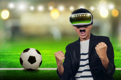 年轻的男人。与耳机虚拟很高兴欢呼的足球游戏与的背景模糊年轻的男人。与虚拟现实耳机