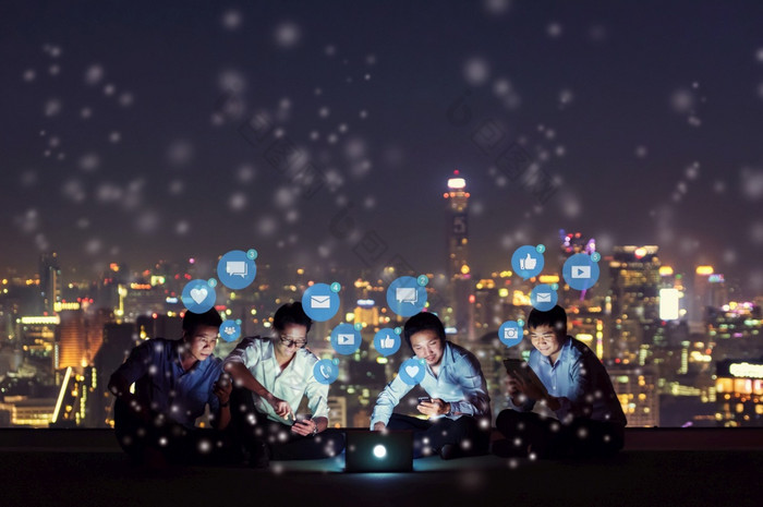 亚洲人集团使用智能手机平板电脑和移动PC为工作玩社会媒体和网站高层屋顶网站与天际线城市晚上社会网络技术概念社会媒体和社会网络