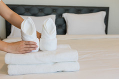 年轻的酒店女仆把软毛巾床上用品和毛巾酒店更清洁的是放置清洁白色毯子的床上与枕头的卧室的早....软毛巾卧室