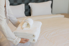 年轻的酒店女仆持有毛巾表和软毛巾的清洁房间的酒店有清洁白色毯子的床上与枕头的早....卧室软毛巾卧室