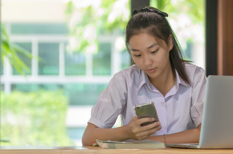 年轻的亚洲大学学生统一的美丽的女孩放松和微笑使用智能手机和移动PC电脑咖啡商店为学习在线休闲业务社会会议教育概念教育概念