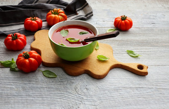 碗新鲜的西班牙冷汤冷番茄汤与罗勒叶子灰色的背景碗新鲜的西班牙冷汤冷番茄汤与罗勒叶子灰色的背景