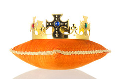橙色皇家天鹅绒枕头与皇冠孤立的在白色背景