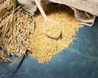 棕色（的）大米未煮过的袋与桩棕色（的）大米与在完整的一匙的量大米和斯派克大米表格背景