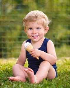 甜蜜的蹒跚学步的婴儿男孩十八岁个月老吃美味的冰奶油在背景与绿色散景户外