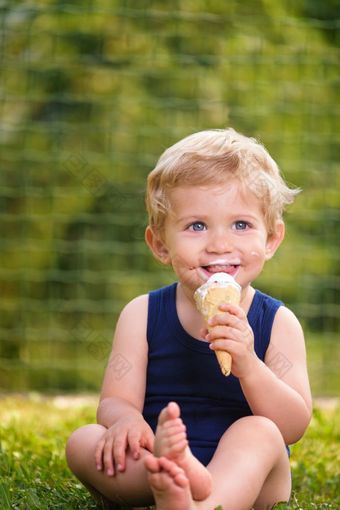 甜蜜的蹒跚学步的婴儿男孩<strong>十八岁</strong>个月老吃美味的冰奶油在背景与绿色散景户外