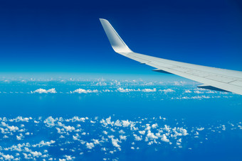 看通过飞机窗口在飞行飞机翼在蓝色的天空和白色cloudscopy空间