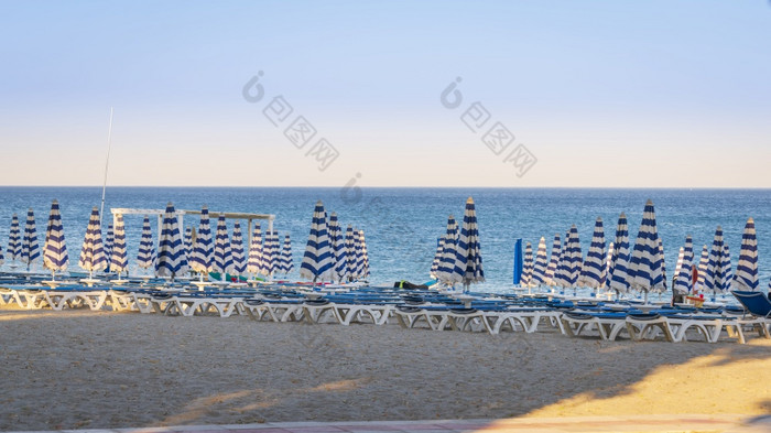 蓝色的和白色伞和海滩椅子的海滩前面蓝色的海和蓝色的天空卡拉布利亚西梅里海意大利