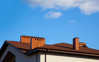 房子与砖烟囱明亮的阳光对深蓝色的天空烟囱的屋顶的房子对的蓝色的天空