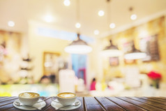 两个咖啡杯棕色（的）木表格在模糊照片美丽的咖啡商店为背景使用
