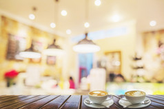 两个咖啡杯棕色（的）木表格在模糊照片美丽的咖啡商店为背景使用