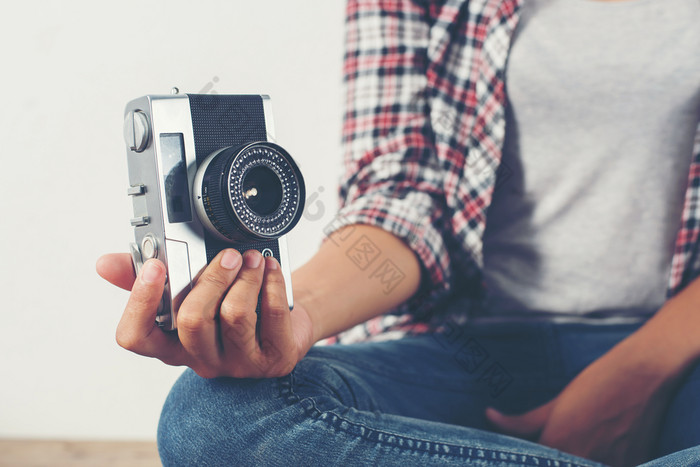 年轻的赶时髦的人摄影师手持有复古的相机坐着年轻的赶时髦的人摄影师手持有复古的相机坐着木地板上