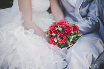 新娘持有婚礼红色的玫瑰花束手的新郎拥抱新娘持有婚礼红色的玫瑰花束手的新郎拥抱他的新娘在一起婚礼情人概念