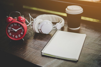 纸杯咖啡笔记本和红色的报警时钟与耳机纸杯咖啡笔记本和红色的报警时钟与耳机的木表格放松时间生活方式概念