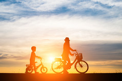 妈妈。与她的孩子骑自行车日落