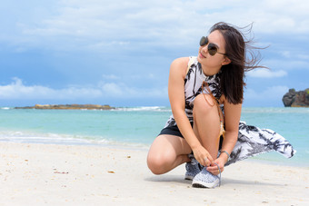 美丽的女人旅游穿sunglasse蹲绑定绳子运动<strong>鞋</strong>的海滩附近的海在的漫步塔鲁陶岛的<strong>夏</strong>天假期satun泰国女人绑定绳子运动<strong>鞋</strong>的海滩泰国