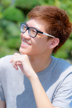 亚洲英俊的十几岁的男孩穿眼镜有趣的肖像快乐的赶时髦的人年轻的男人。是微笑和笑与快乐脸公园绿色自然背景泰国亚洲有趣的十几岁的男孩穿眼镜