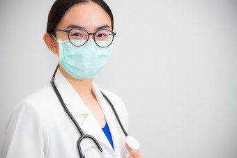 工作室肖像美丽的亚洲年轻的女人医生与听诊器白色统一的穿眼镜和绿色面具保护电晕病毒为健康看相机灰色的复制空间背景女人医生与听诊器灰色的背景