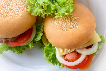 特写镜头前视图两个芝士汉堡使从猪肉牛肉绿色生菜面包洋葱白色芝麻和番茄白色板表格背景使首页汉堡美味的美国快食物前视图两个汉堡白色板