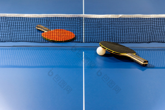 黑色的和红色的表格网球球拍和白色球的蓝色的平发出难闻的气味表格与网两个表格网球桨体育竞争设备室内活动和锻炼为背景概念黑色的和红色的表格网球桨与网